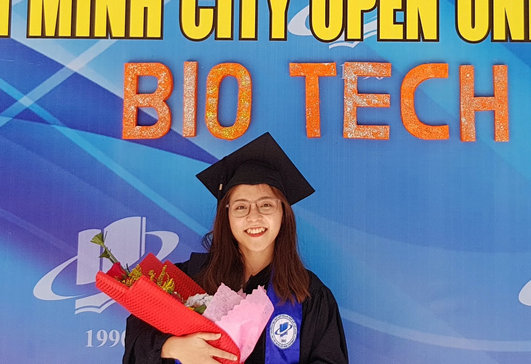 A young woman graduate in cap and gown holding flowers